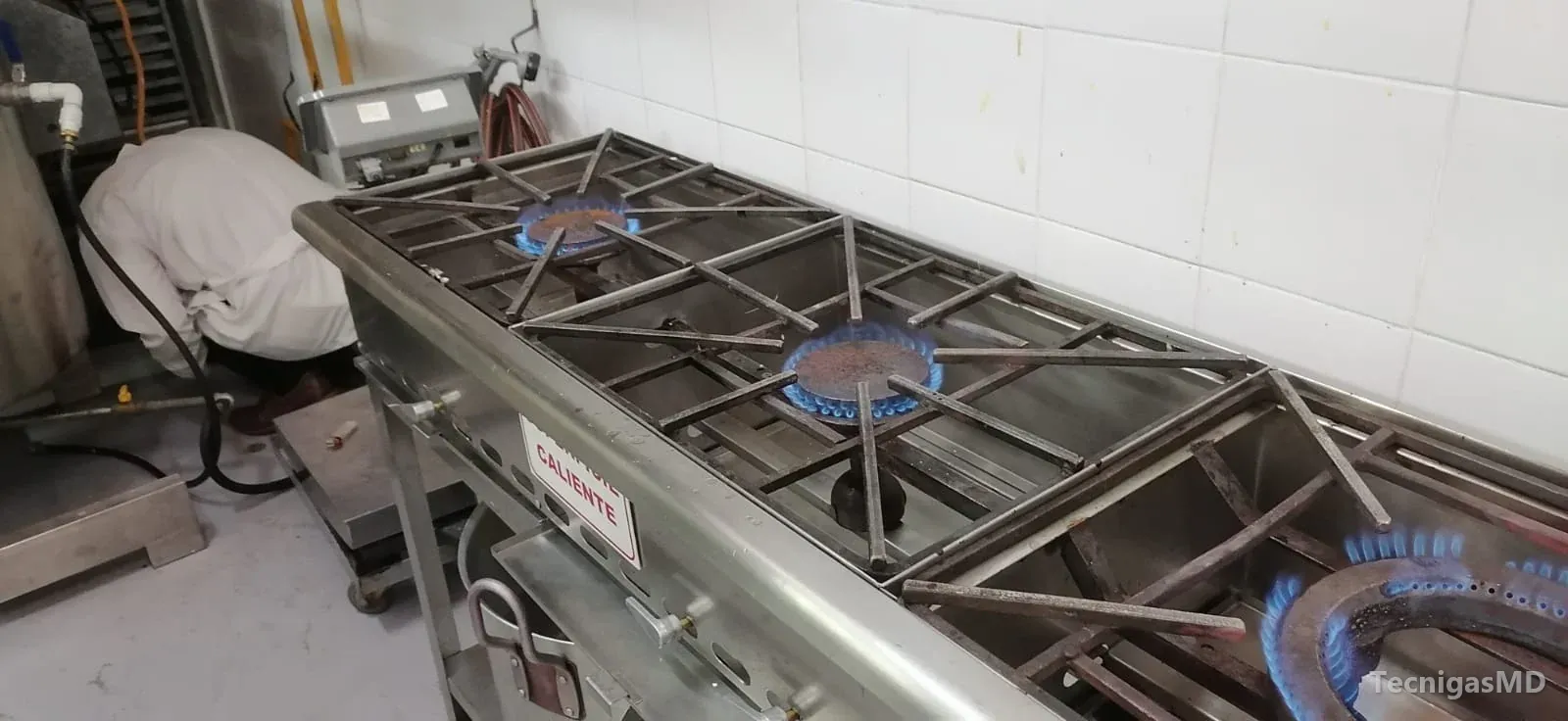 Estufa industrial a gas en acero inoxidable con quemadores de llama azul encendidos en una cocina comercial